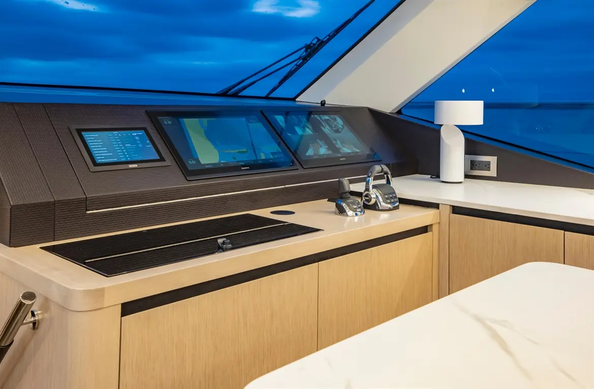 Modern yacht helm with multiple screens displaying navigation data, sleek controls, wooden cabinetry, and a lamp.